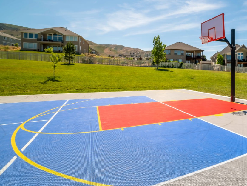 Public Basketball Court in Open Park with Houses in the Background on Sunny Day